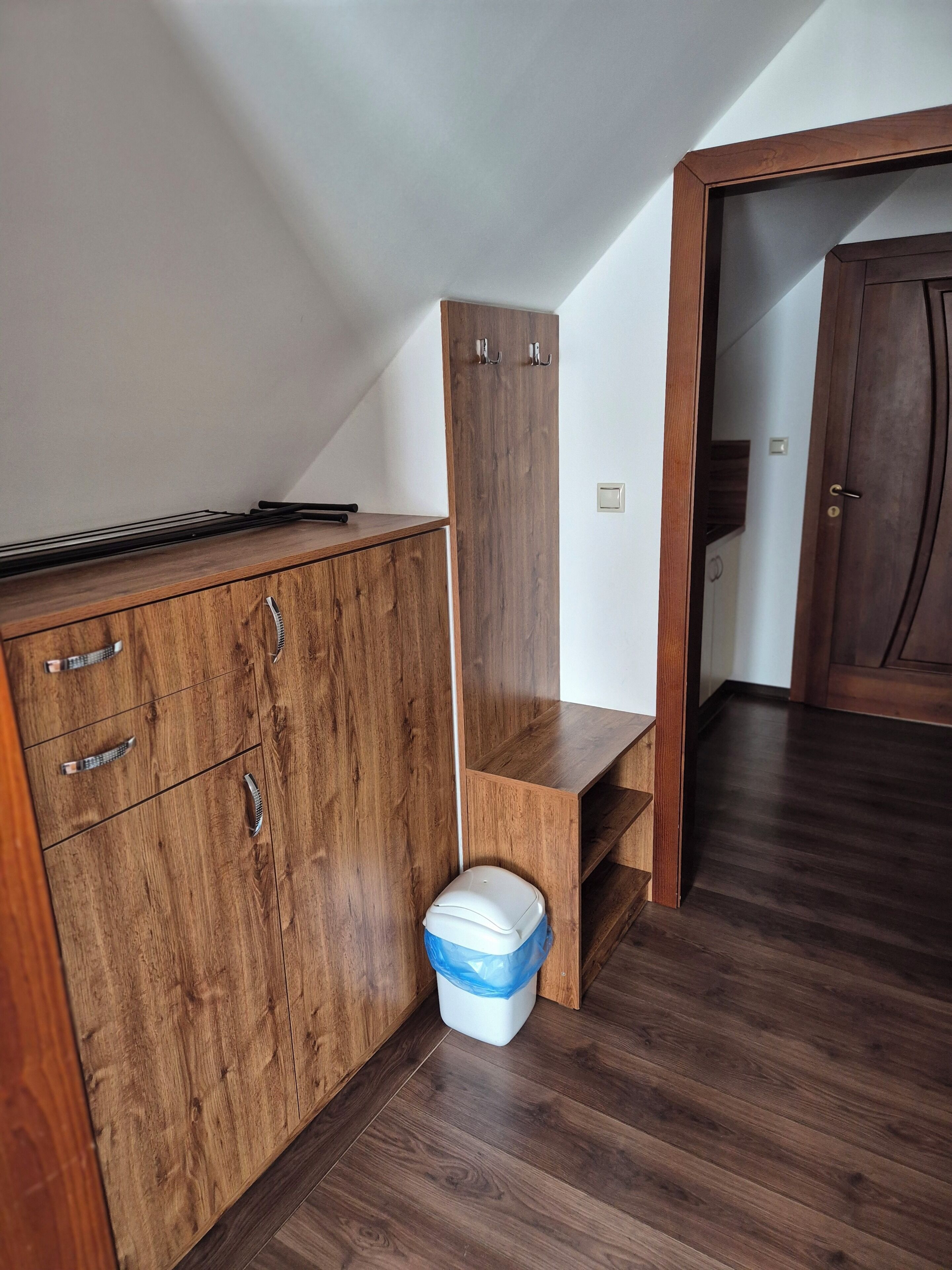 Una habitación con un armario de madera, un cubo de basura y una puerta que da a otra habitación.