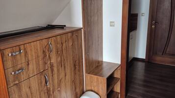 Una habitación con un armario de madera, un cubo de basura y una puerta que da a otra habitación.