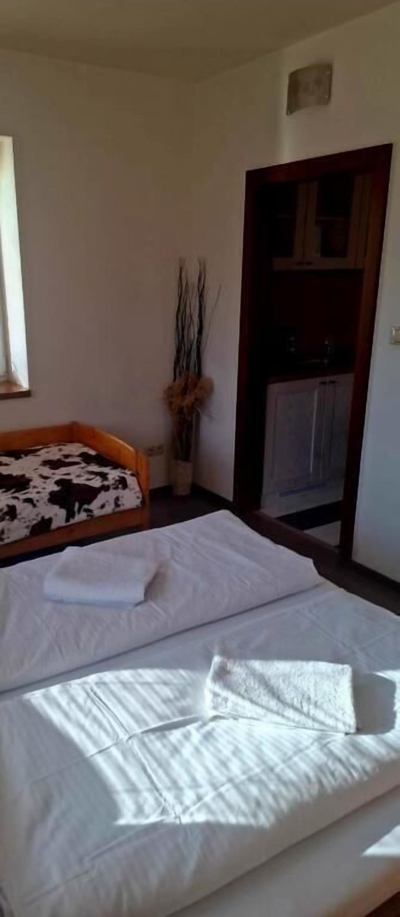 Una habitación con una cama, una mesita con un florero y una puerta que da a una cocina.