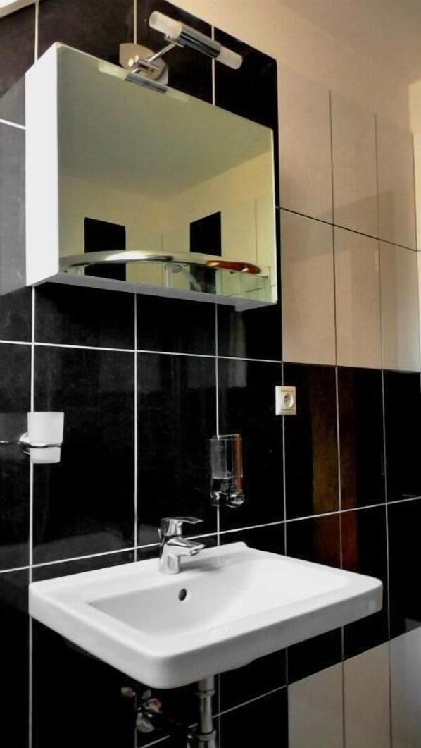 A bathroom with a white sink, a mirror, and black tiles.