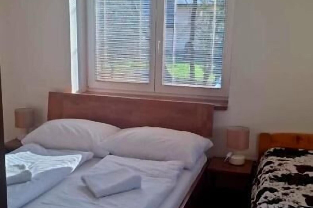 Un dormitorio con cama, mesita de noche y ventana con persianas.
