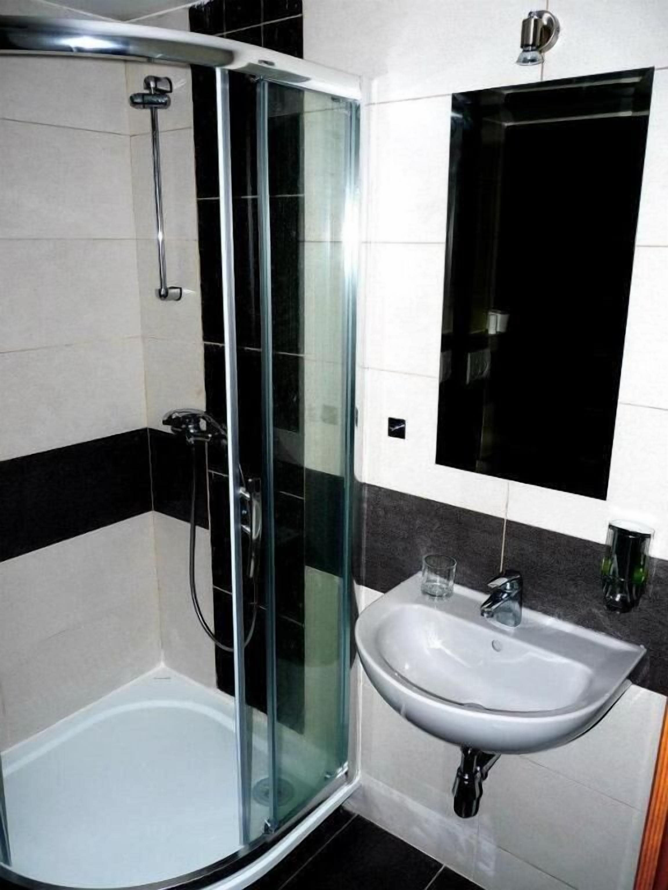 Casa de banho com chuveiro em cabine de vidro, lavatório branco e parede revestida a mosaico preto e branco.