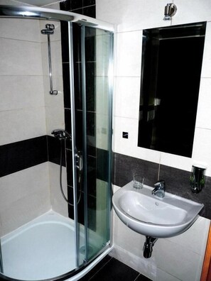 Un baño con cabina de ducha de vidrio, un lavabo blanco y pared con baldosas blanco y negro.