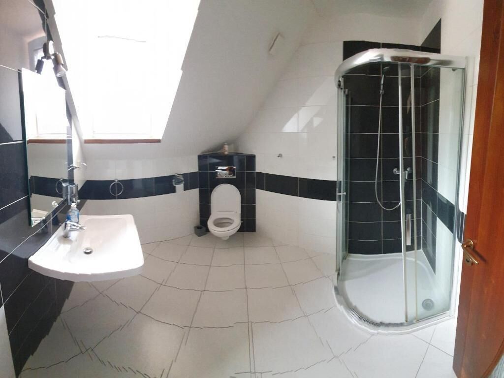 Un baño con lavamanos blanco, inodoro, cabina de ducha y tragaluz.