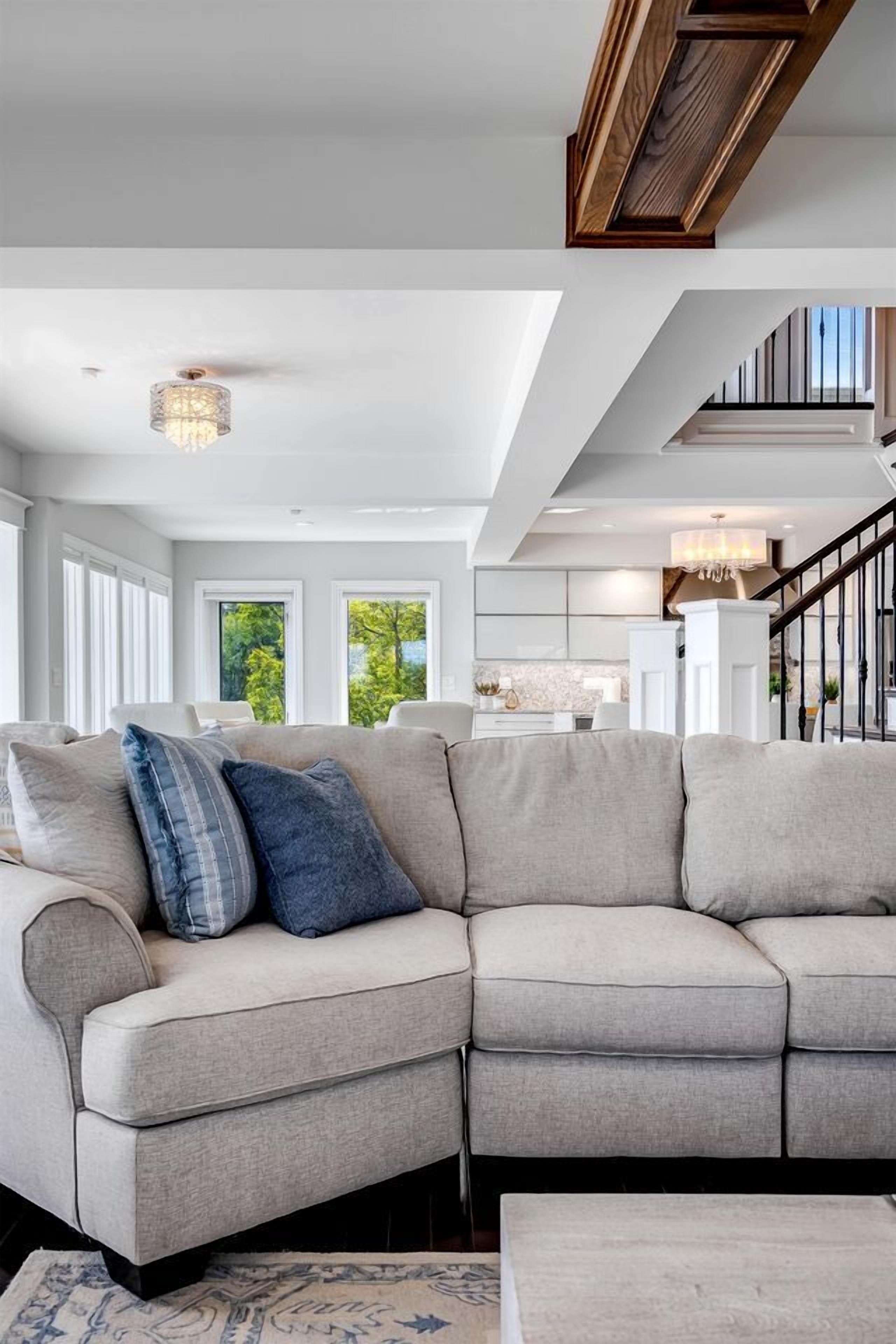 Ein modernes Wohnzimmer mit einem Ecksofa, einer Deckenleuchte und einer Treppe, die in eine obere Ebene führt.