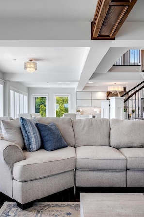 A modern living room with a sectional sofa, a chandelier, and a staircase leading to an upper level. - Luxury Waterfront Estate with Beach Access and Expansive Grounds in Ontario, Canada (Wheatley)