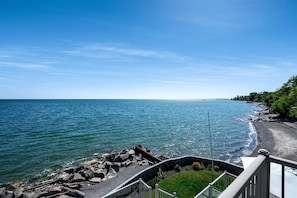 A coastal view with a clear sky, a rocky shoreline, and a grassy area with a railing. - Luxury Waterfront Estate with Beach Access and Expansive Grounds in Ontario, Canada (Wheatley)