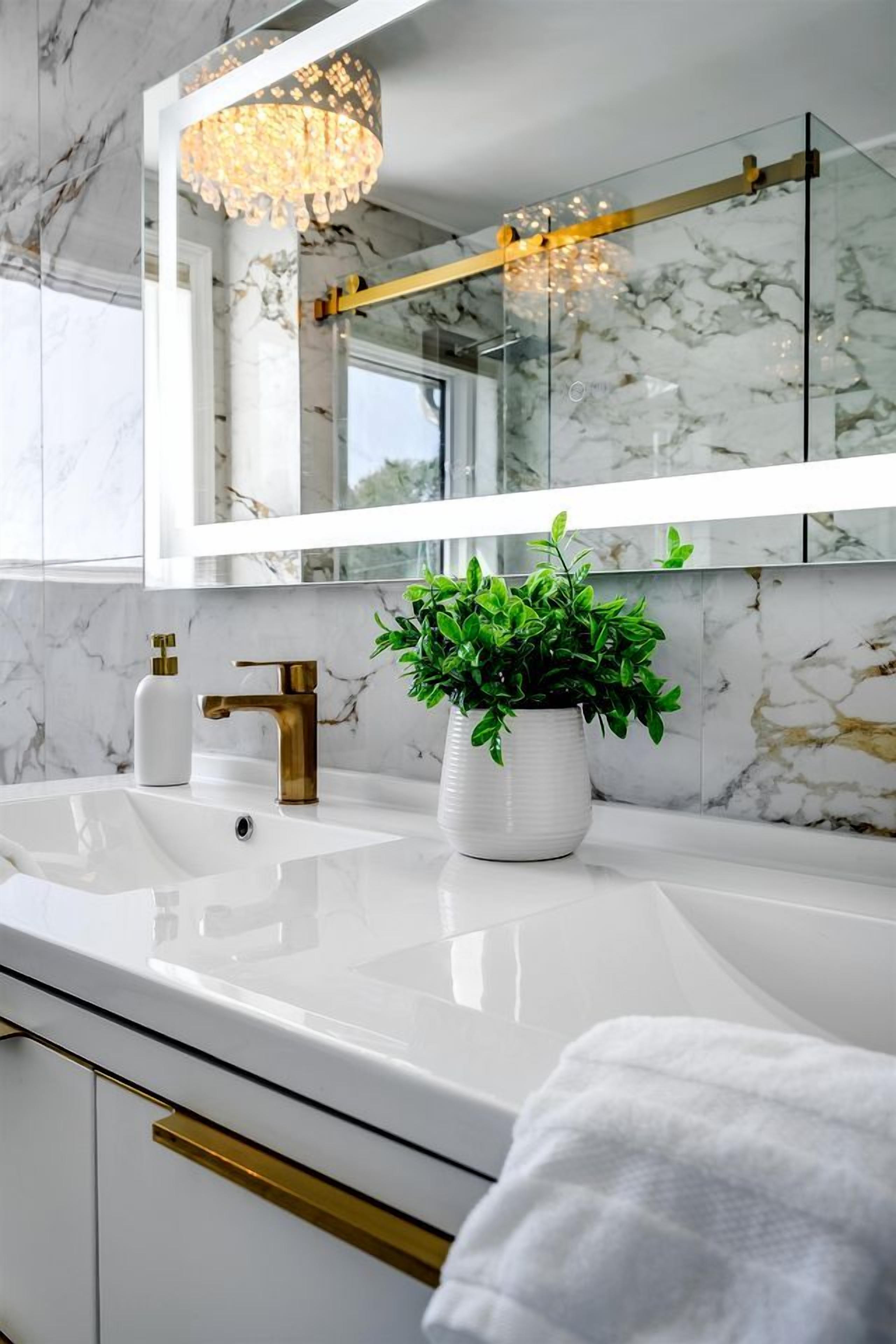 A bathroom with a white marble sink, gold faucet, and a potted plant.