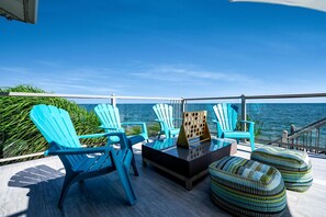 A deck with blue Adirondack chairs, a glass-top table, and patterned ottomans. - Luxury Waterfront Estate with Beach Access and Expansive Grounds in Ontario, Canada (Wheatley)