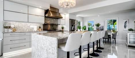 A modern kitchen with a marble island, bar stools, and a large window.