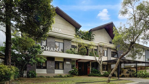 Un hotel moderno con entrada cubierta, un cartel con el nombre y un jardín bien cuidado.