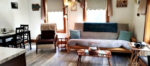 Ein gemütliches Blockhauss-Interieur mit einer Couch, einem Esstisch, Stühlen und einer kleinen Küchenzeile.