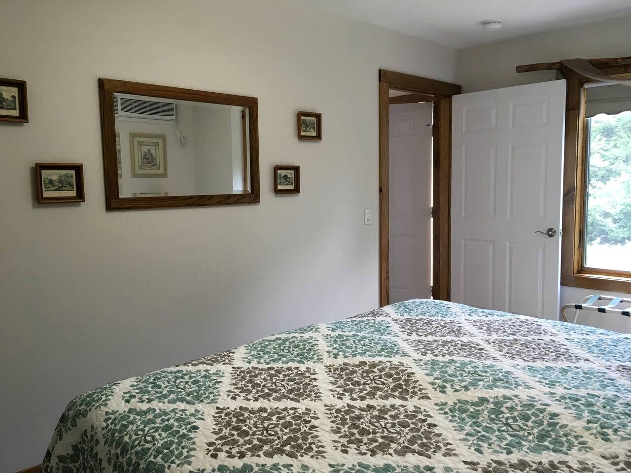 Um quarto com uma cama, um espelho grande e uma porta que dá para outro cômodo.