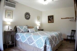 Quarto com cama, duas mesas de cabeceira com luminárias, uma cadeira, aquecedor fixado na parede e um porta-retrato.