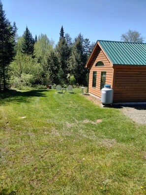 Eine kleine Holzhütte mit einem grünen Dach, umgeben von einem grasbewachsenen Hof und dichtem Wald.