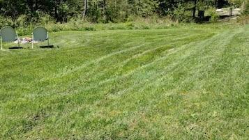 Een verzorgd grasveld met enkele stoelen en een bankje, omringd door bomen.