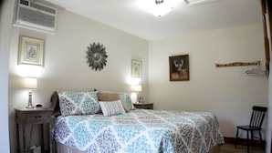 Quarto com cama, duas mesas de cabeceira com luminárias, uma cadeira, aquecedor fixado na parede e um porta-retrato.