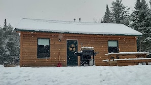 Uma cabana de madeira com telhado coberto de neve, porta da frente e um pequeno alpendre.