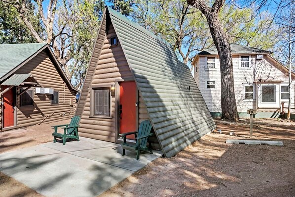 A log cabin with a steeply pitched roof, a small porch with two green Adirondack chairs, and a red door. - Rustic A-Frame Cabins with Modern Amenities near Garden of the Gods in Colorado Springs, Colorado (Colorado Springs)