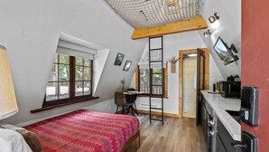 Ein Schlafzimmer mit erhöhtem Schlafbereich, einem Schreibtisch und einer Küchenzeile.