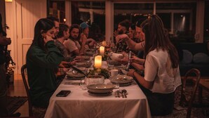 Un grupo de personas cenando en una mesa con velas, rodeado de luces de cadena.