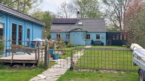 Uma casa azul com telhado de metal, cerca de madeira e um caminho pavimentado.