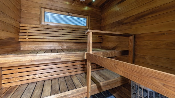 A wooden sauna with benches, a window, and a ceiling vent.