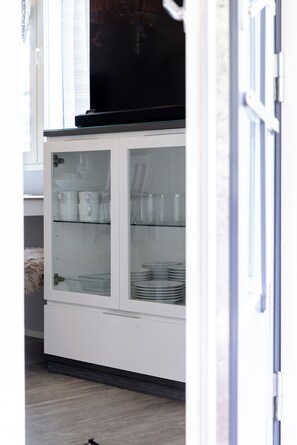 A white cabinet with glass doors containing plates and cups.