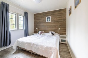 A bedroom with a wooden headboard, a large bed with white bedding, two bedside lamps, and a window with curtains.