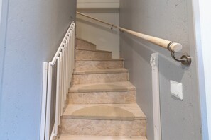 A staircase with a wooden handrail, white balusters, and a door with a light switch.