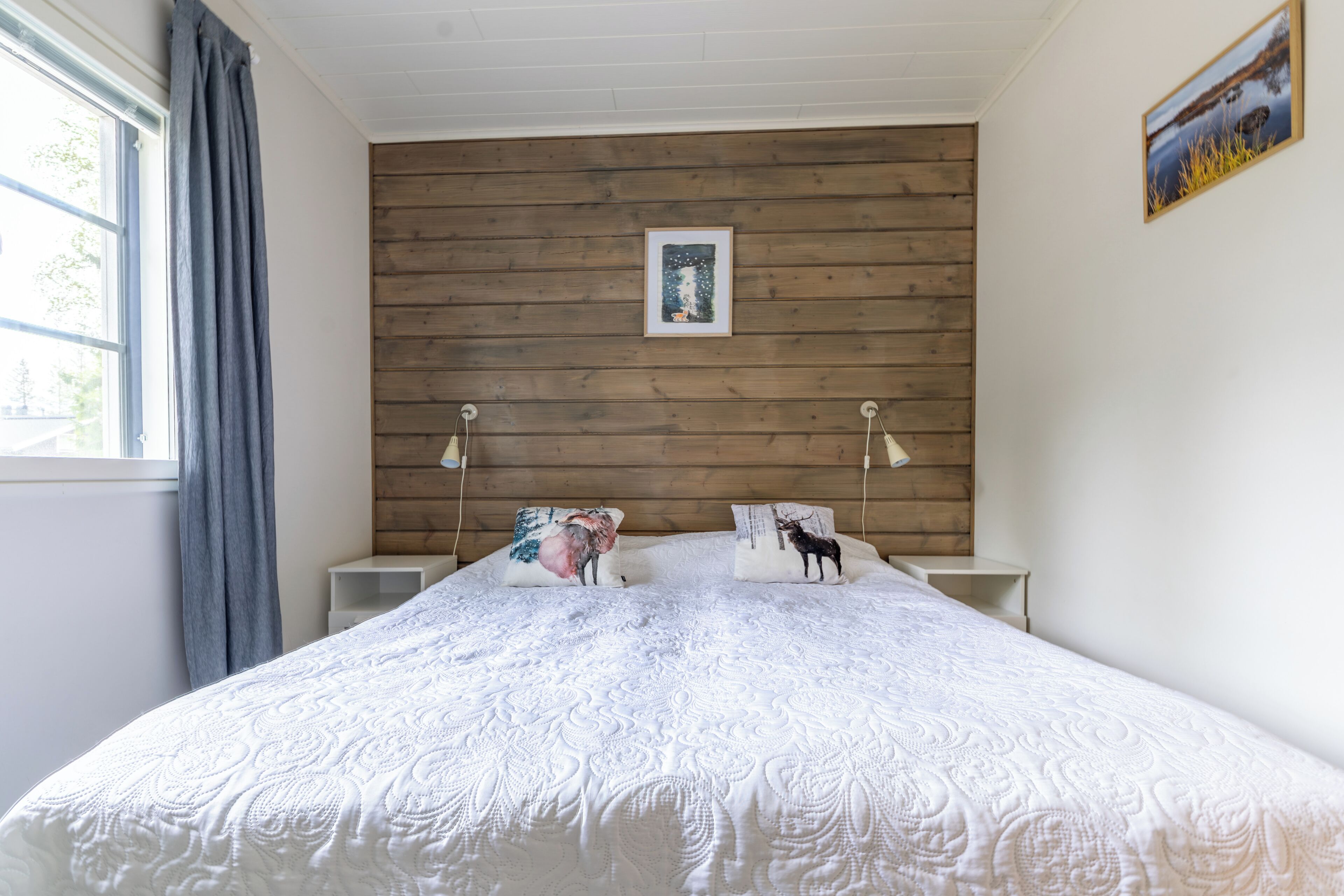 Ein Schlafzimmer mit einem hölzernen Kopfteil, einer weißen gesteppten Bettdecke, zwei Nachttischlampen und einem gerahmten Bild an der Wand.