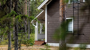 A wooden cabin with a porch, surrounded by trees.