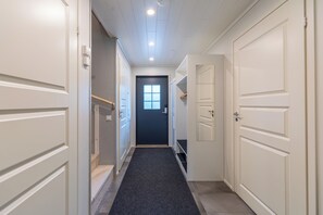 A hotel hallway with white doors, a dark carpet, and a window at the end.