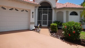 Ein Wohnhaus mit Garage, Eingangstür und einem kleinen Garten mit Pflanzen und einem Vogel.
