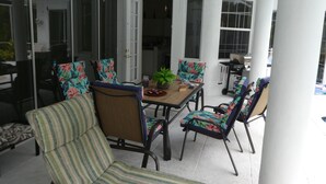 Ein überdachter Patio-Bereich mit Tisch und Stühlen, einem Deckenventilator und einer Schiebetür zu einem Innenraum.