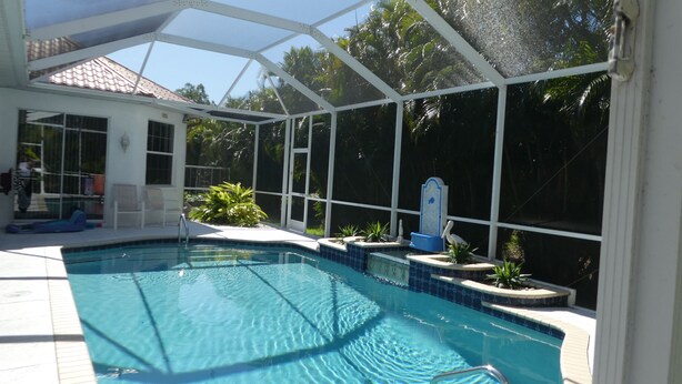 Ein überdachter Pool mit freiem Blick auf die Umgebung, darunter ein Haus mit einem Ziegeldach und einem eingezäunten Garten.