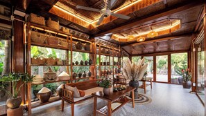 A room with wooden furniture, shelves with pottery, and a ceiling fan. - The Boi Heritage Tam Coc (Hoa Lu)