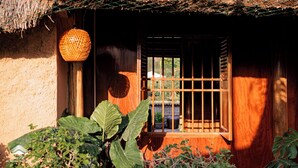 A rustic building with a thatched roof, a wooden door with a metal bar, and large green foliage in the foreground.