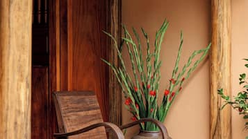 A wooden chair and a vase with plants and red flowers on a stone-paved porch.