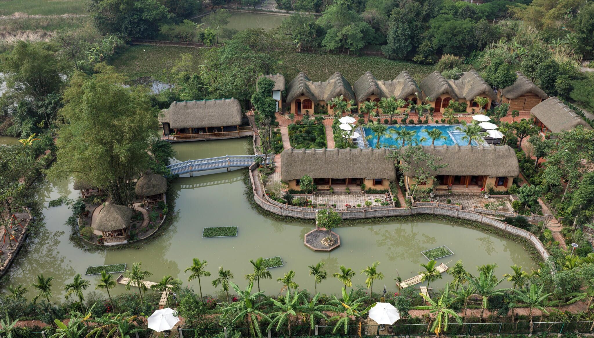 A resort with thatched-roof buildings, a central pool, and a surrounding water body.