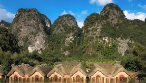 A row of traditional thatched-roof cottages with a mountainous backdrop. - The Boi Heritage Tam Coc (Hoa Lu)
