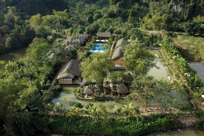 Un resort con estructuras de techo de paja, piscina y un paisaje natural circundante.