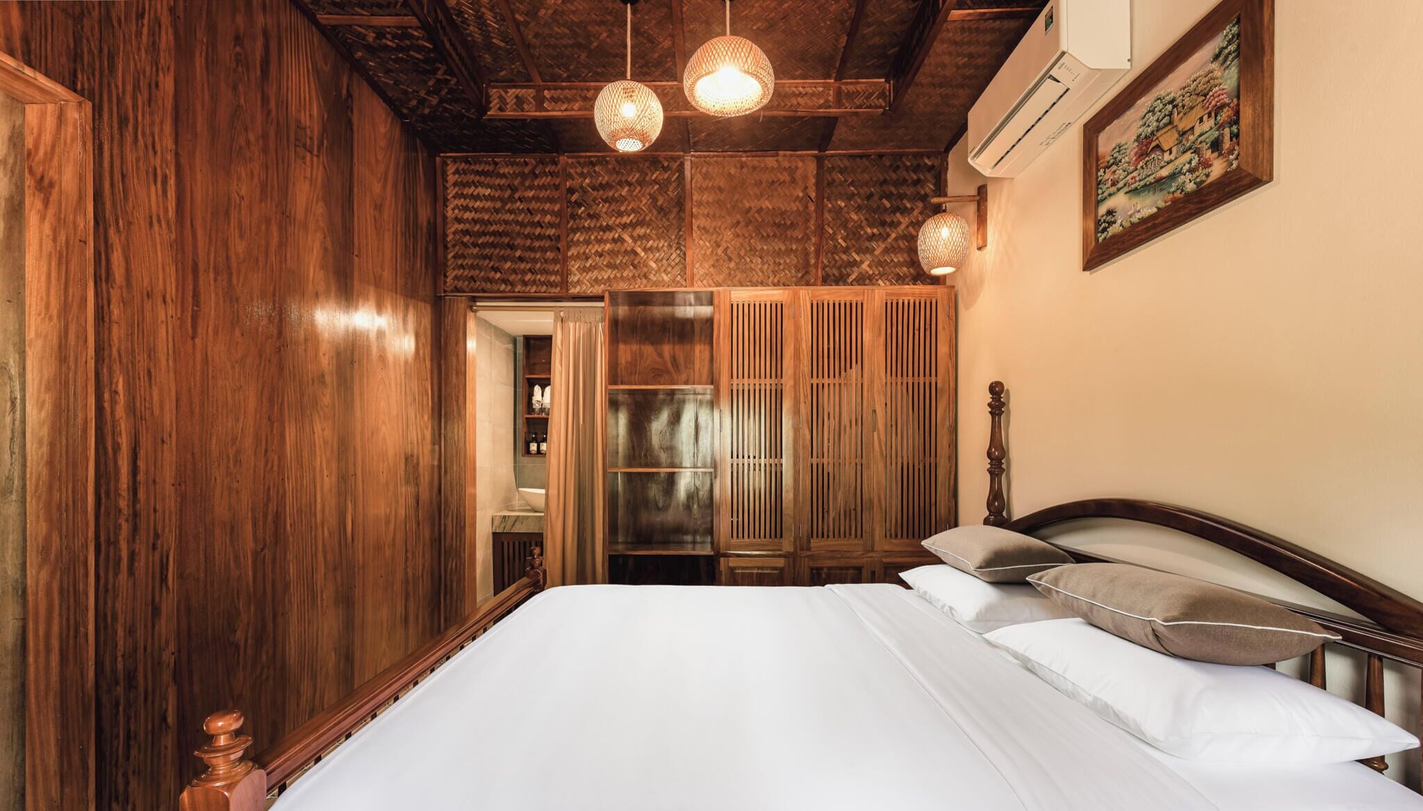 A bedroom with a wooden wardrobe, a bed with white bedding, and a hanging light fixture.