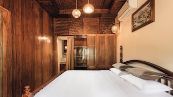 A bedroom with a wooden wardrobe, a bed with white bedding, and a hanging light fixture.