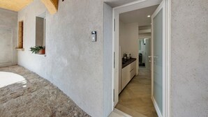 A modern interior with a concrete wall, a potted plant, a built-in shelf, and a doorway leading to a kitchen area. - Apartment 'Nora' with Shared Garden, Wi-Fi and Air Conditioning (Polpenazze del Garda)