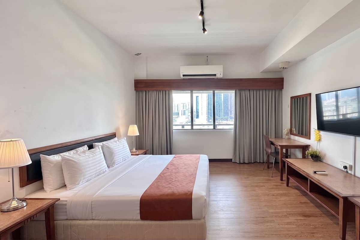 Una habitación de hotel con cama, mesitas de noche, escritorio, televisor y ventana con cortinas.