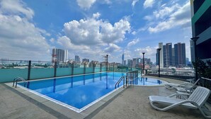 A rooftop pool with a city skyline view, lounge chairs, and a clear sky.