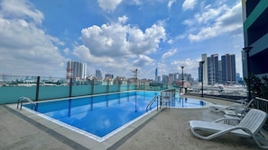 Una piscina en la azotea con vistas al horizonte de la ciudad, sillas de descanso y cielo despejado.