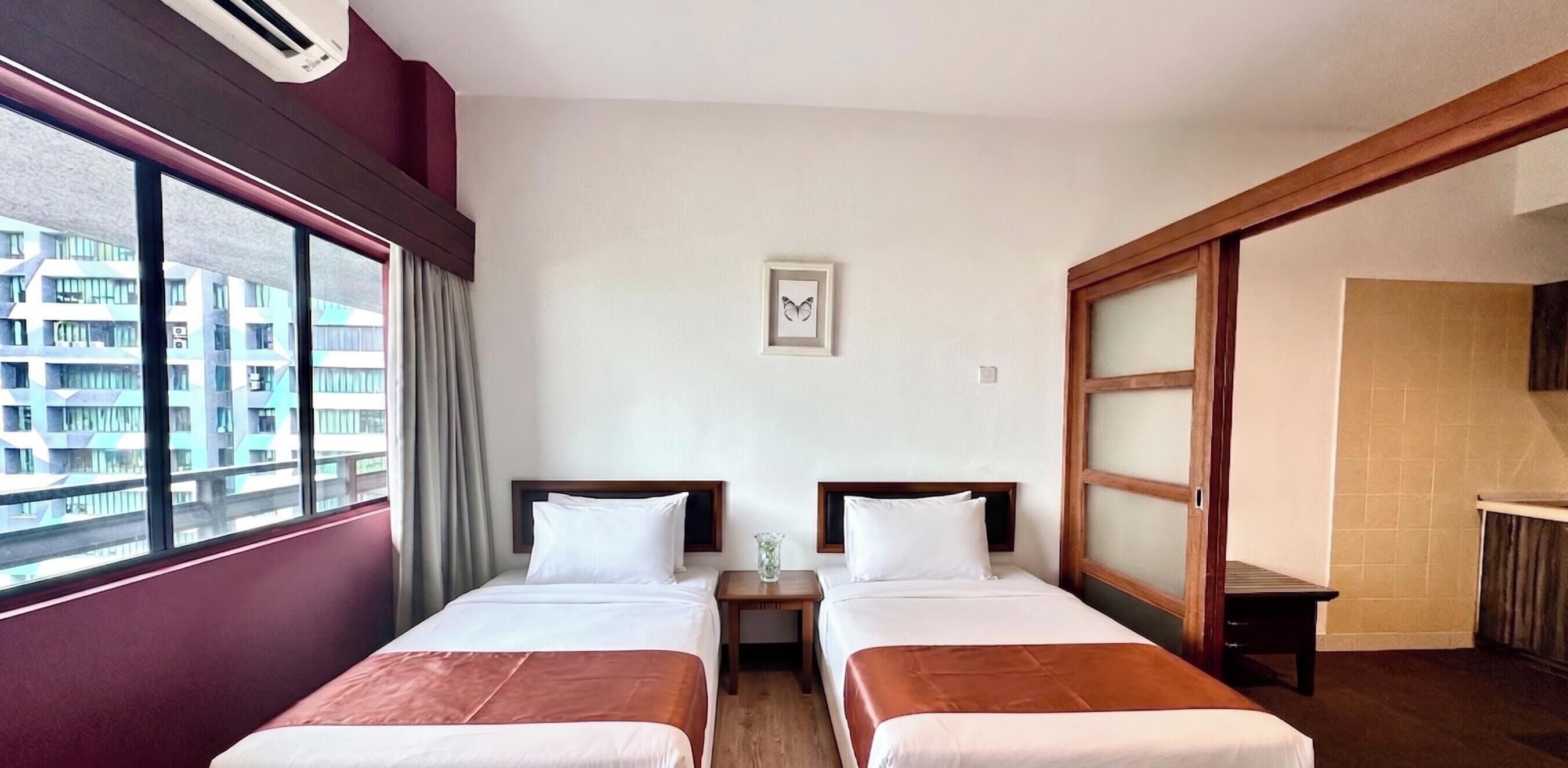 Una camera d'albergo con due letti, una finestra vista edifici, un tavolino e un quadro appeso al muro.
