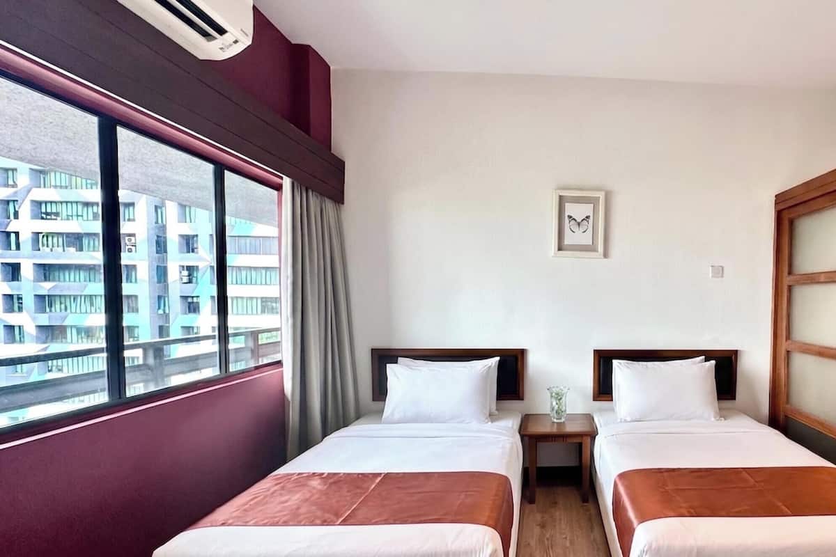 Habitación de hotel con dos camas, una ventana con vista a edificios, una mesita pequeña y un cuadro en la pared.